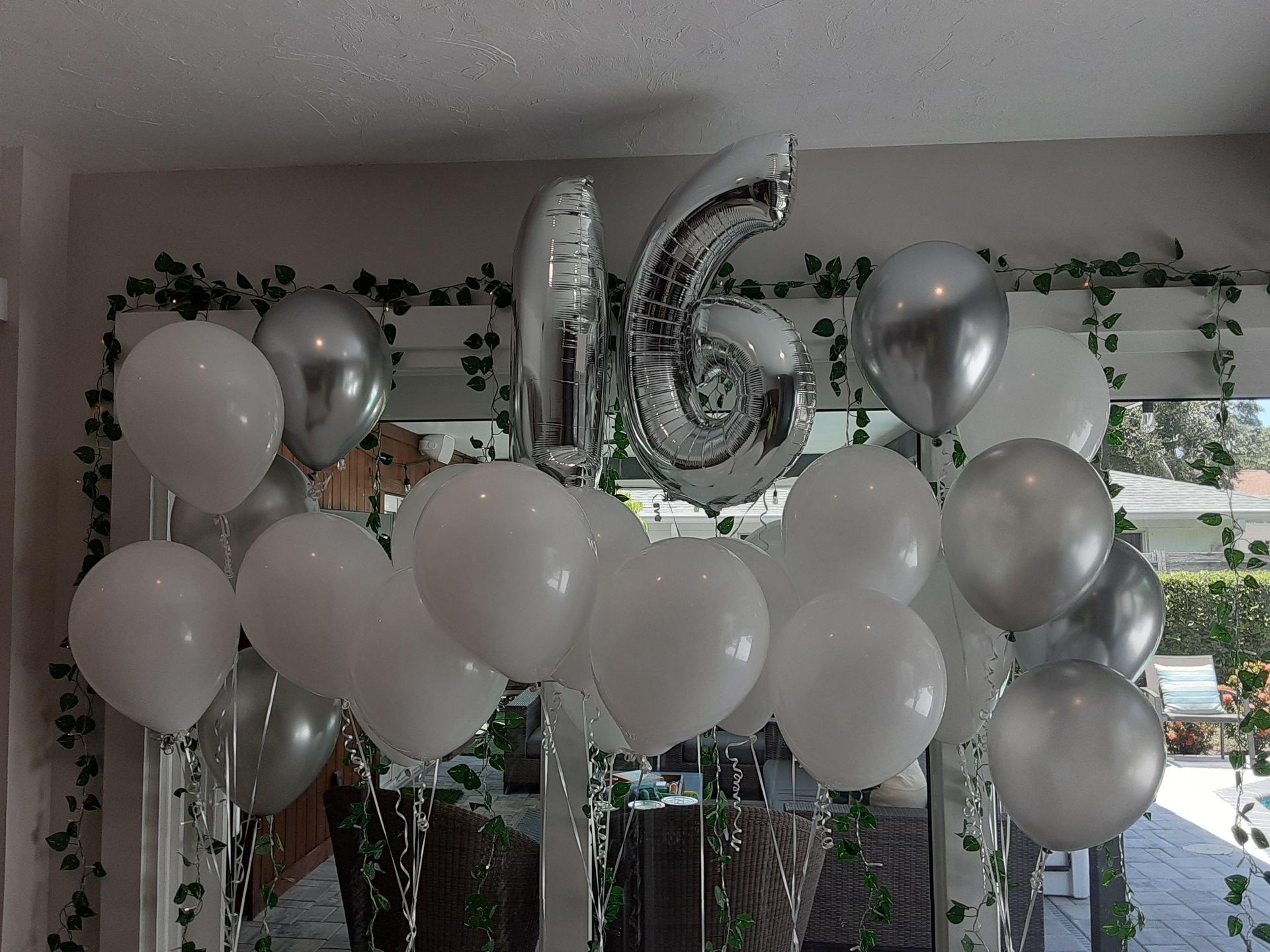 A bunch of white and silver balloons with a silver number 6 hanging from the ceiling