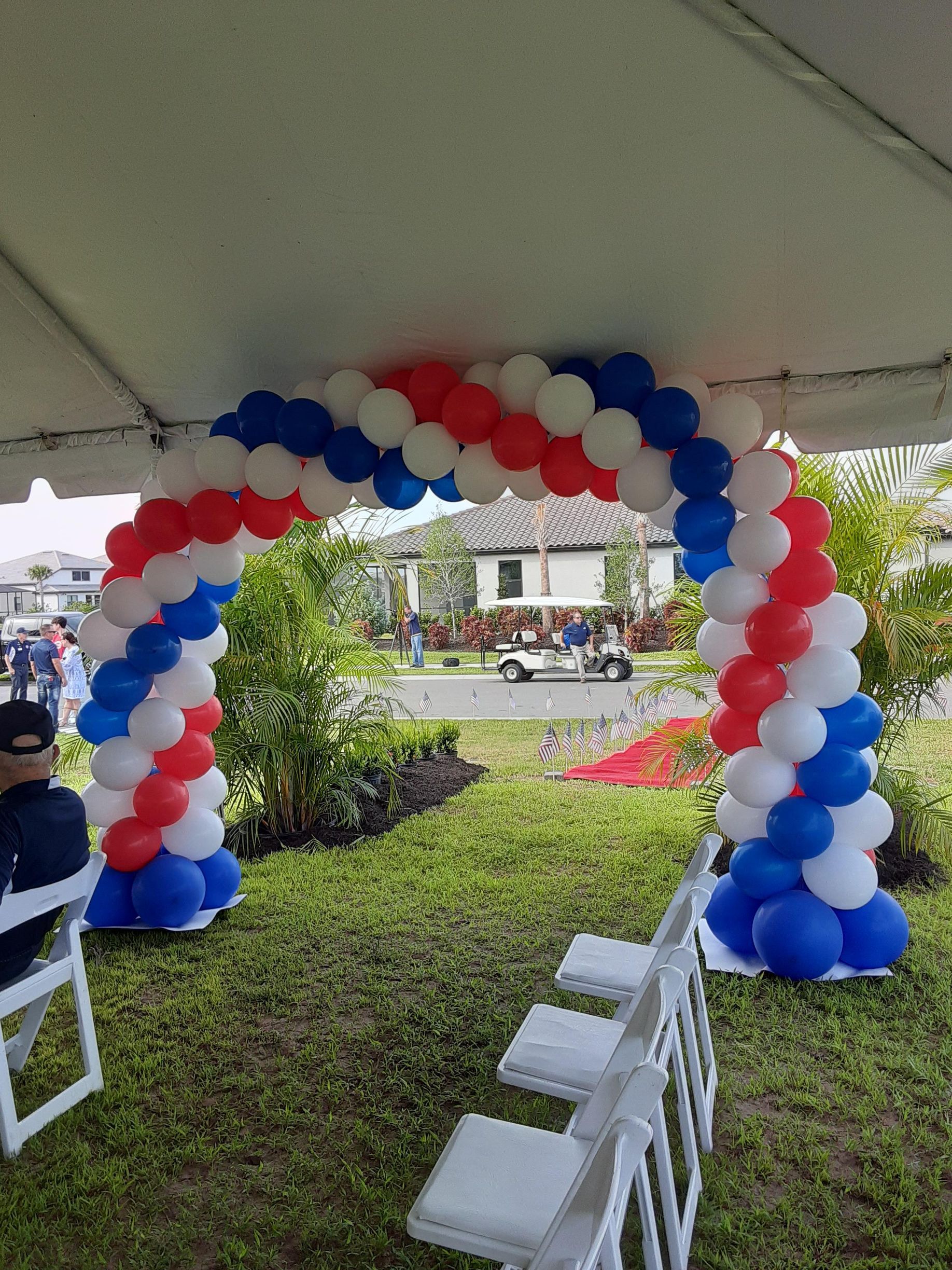 A red , white and blue balloon arch is sitting under a tent.