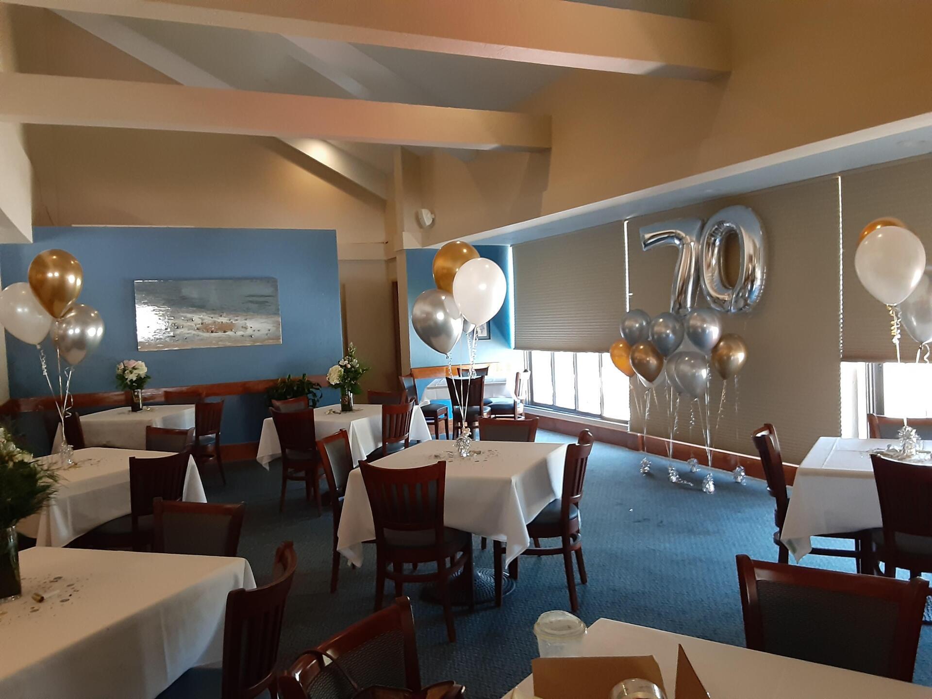 A restaurant with tables and chairs and balloons with the number 70 on the wall