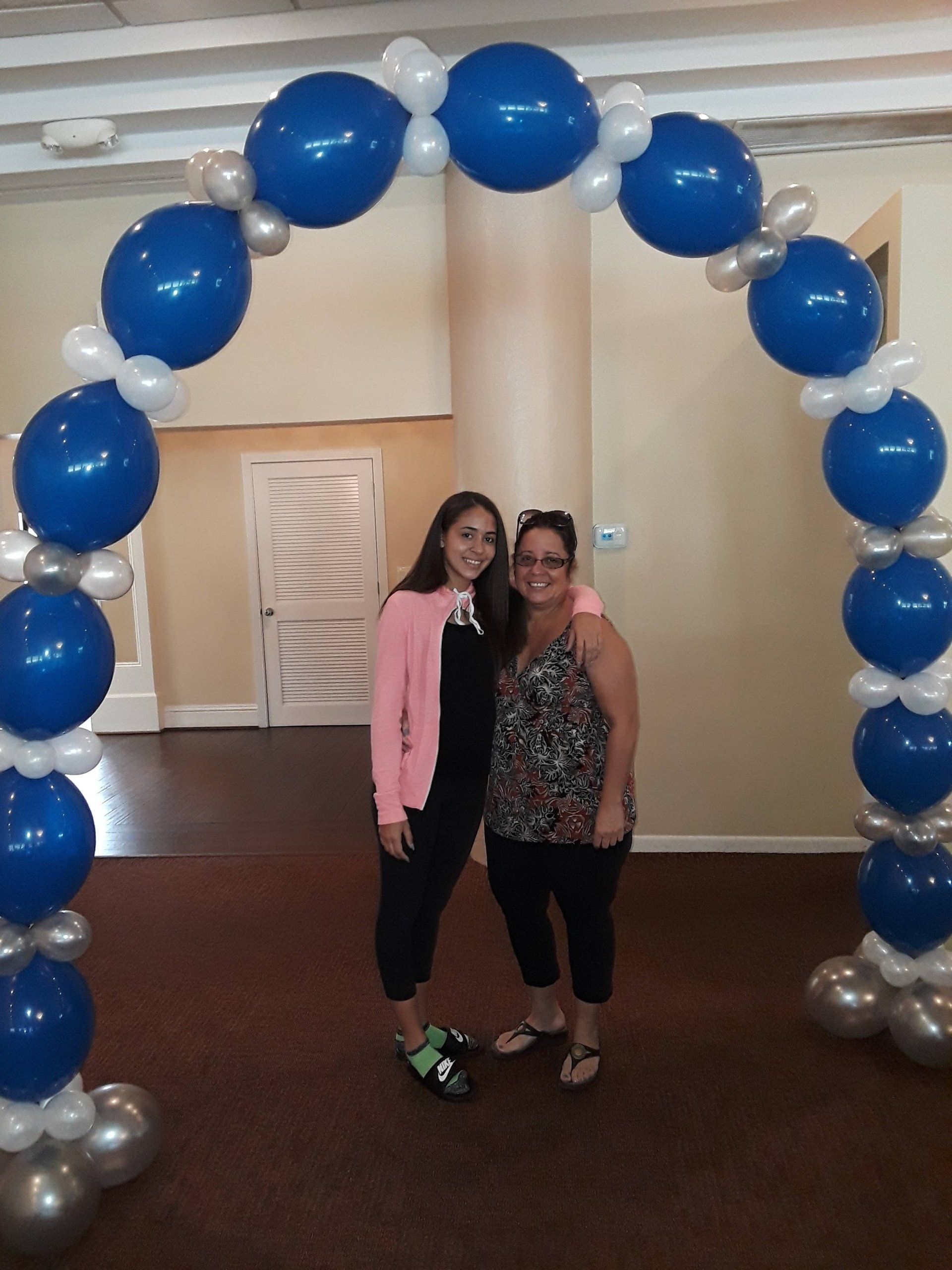 Two women standing under a blue and silver balloon arch