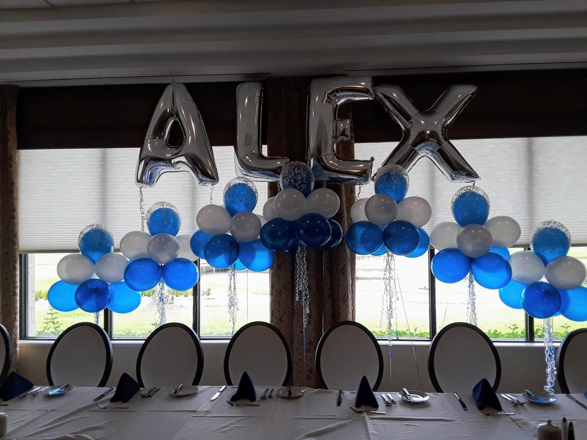 A table is decorated with blue and white balloons and the name alex