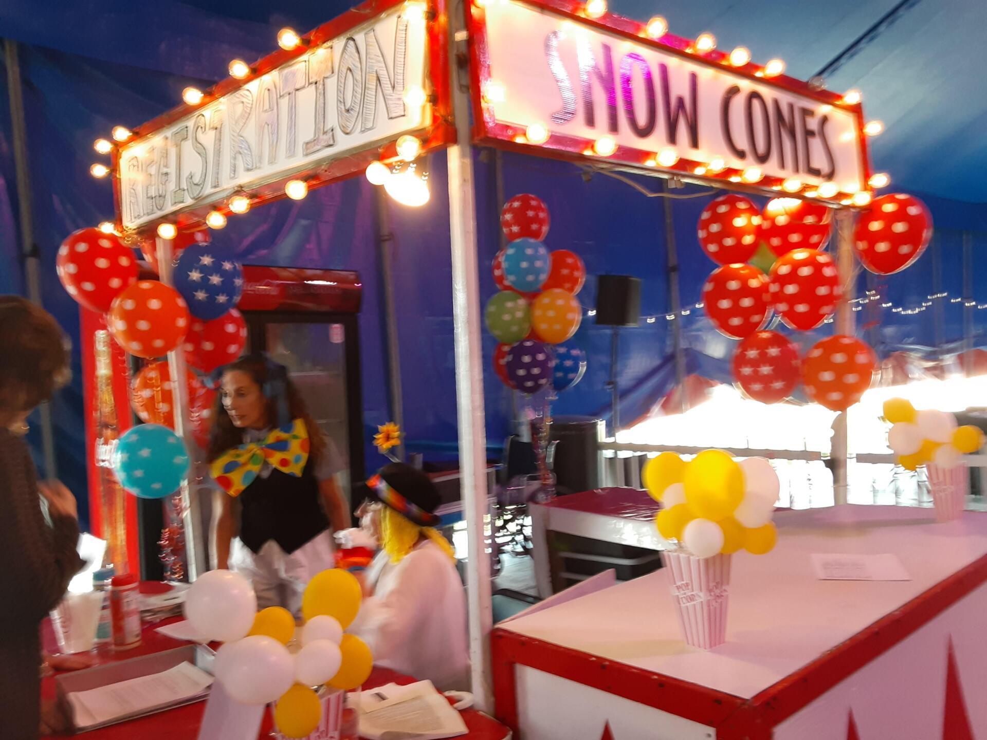 A snow cone stand is decorated with balloons and lights