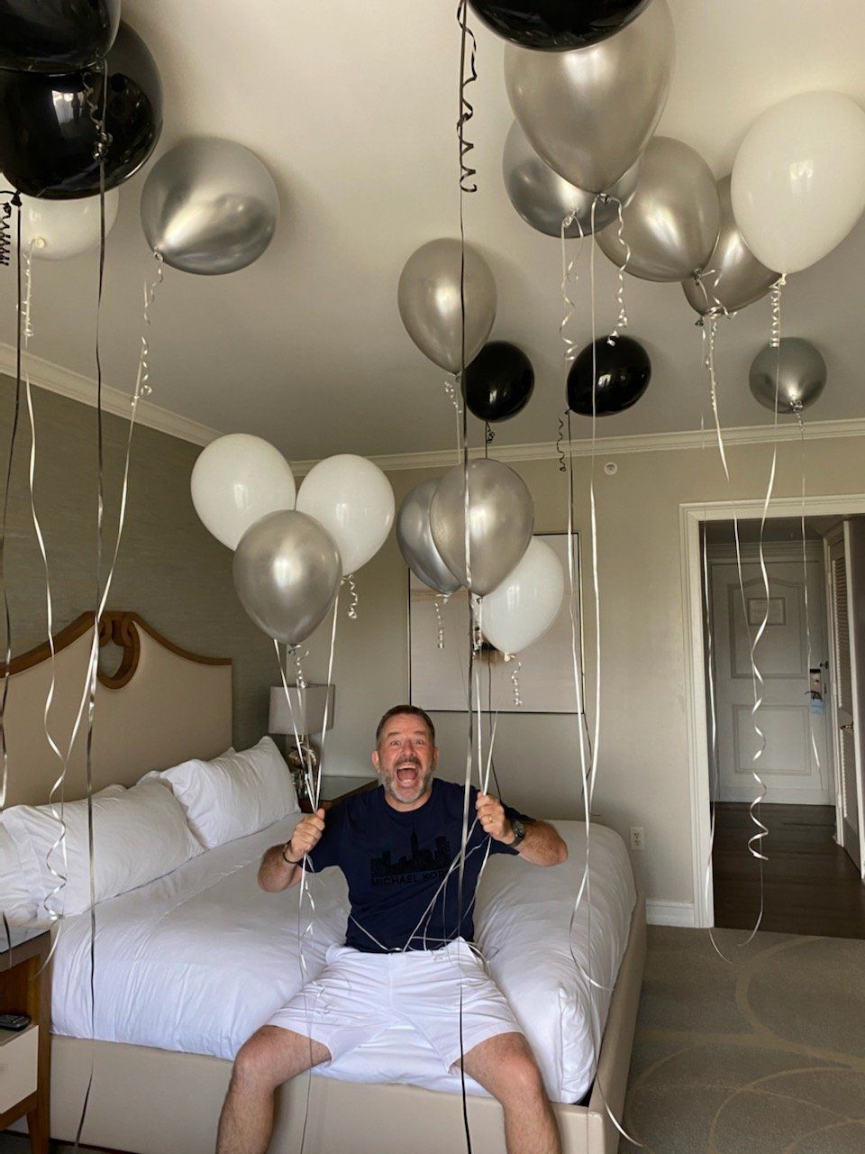 A man is sitting on a bed with balloons hanging from the ceiling