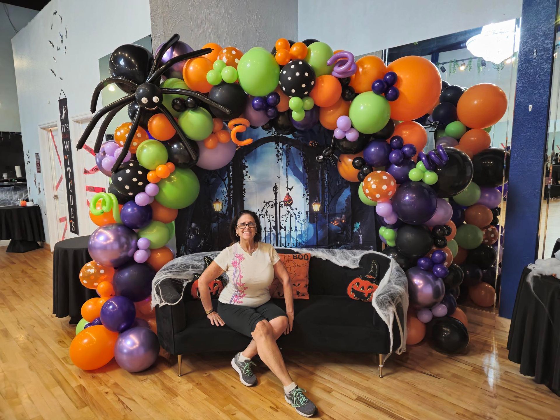 A woman is sitting on a couch in front of a balloon arch.
