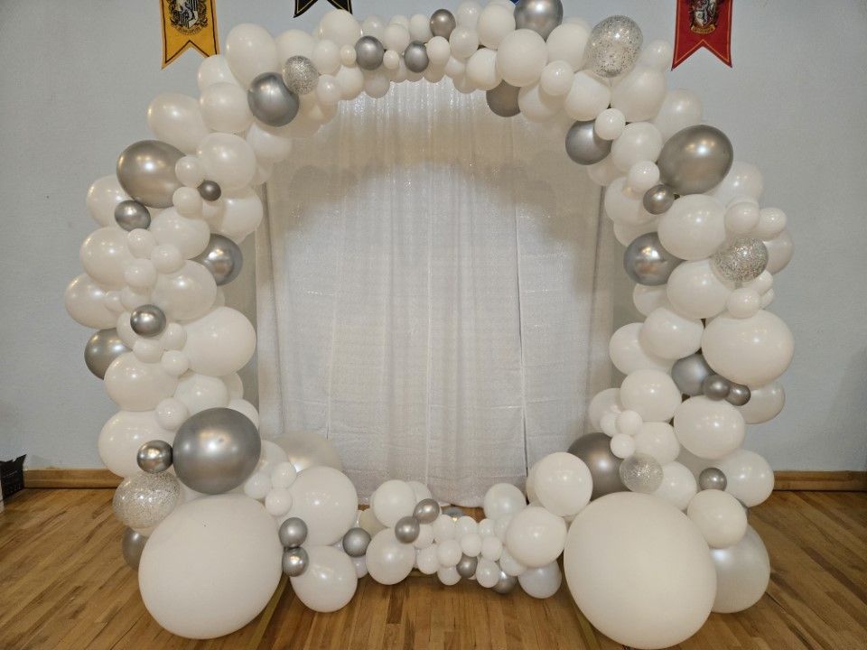 A white and silver balloon arch is sitting on a wooden floor.