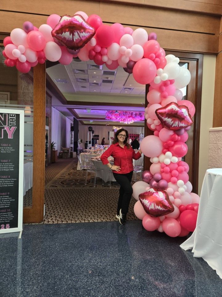 A woman is standing in front of a pink balloon arch