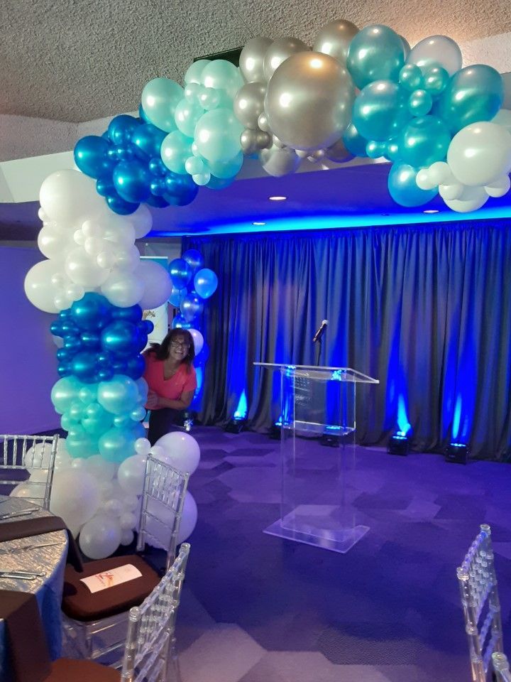 A woman is standing in front of a podium decorated with blue and white balloons.