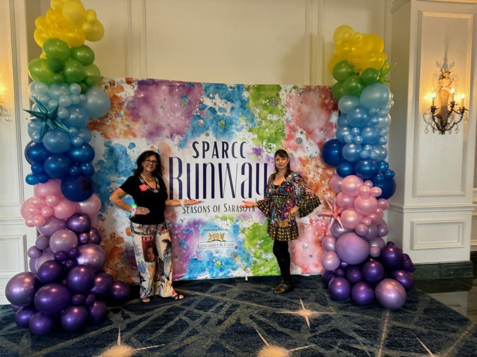 Two women are standing in front of a wall covered in balloons.