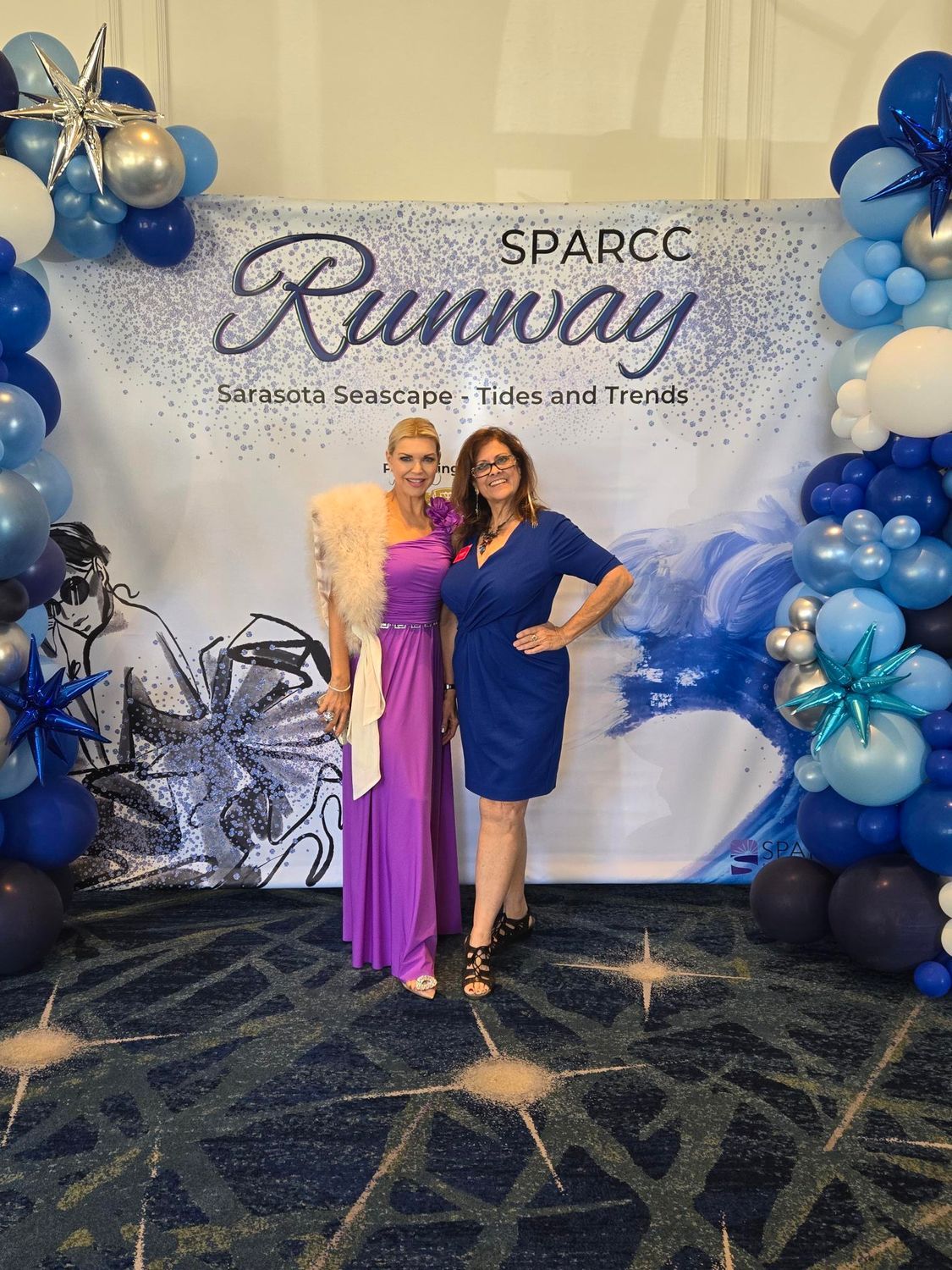 Two women pose in front of a SPARCC Runway backdrop with balloons.