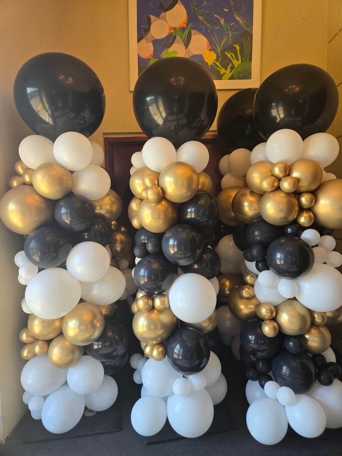 Three balloon columns with black, white, and gold balloons topped with large black balloons.