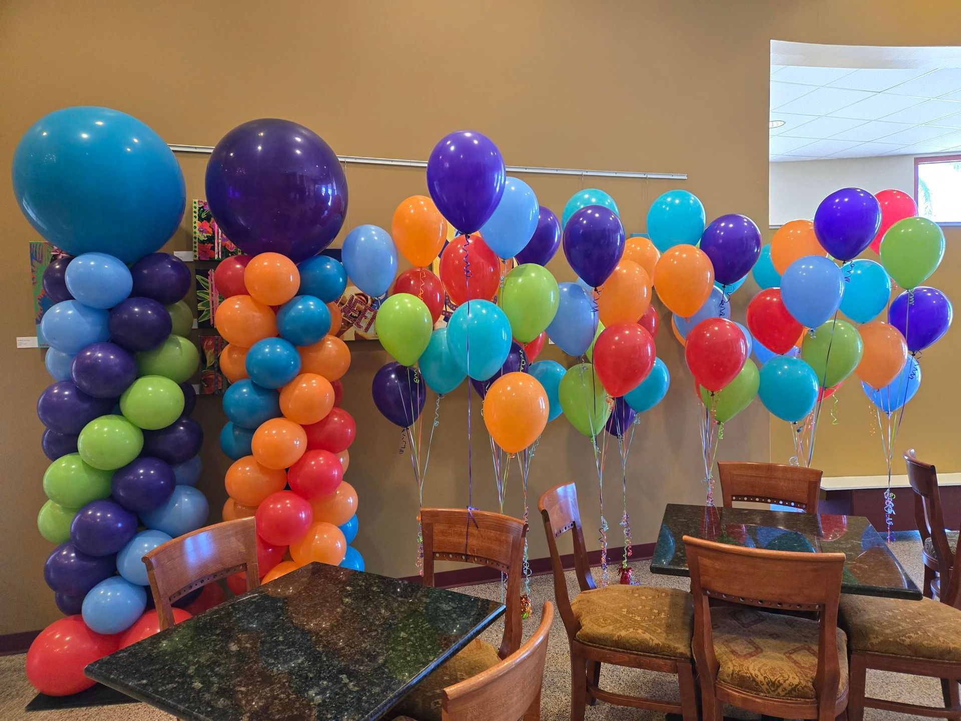 Colorful balloon display in a dining area. It features a column of balloons and several clusters of floating balloons in various colors.