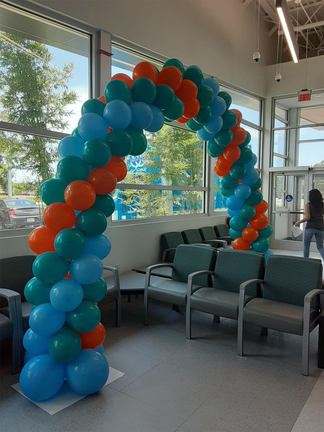 A balloon arch in teal, orange, and blue frames an entrance with seating.