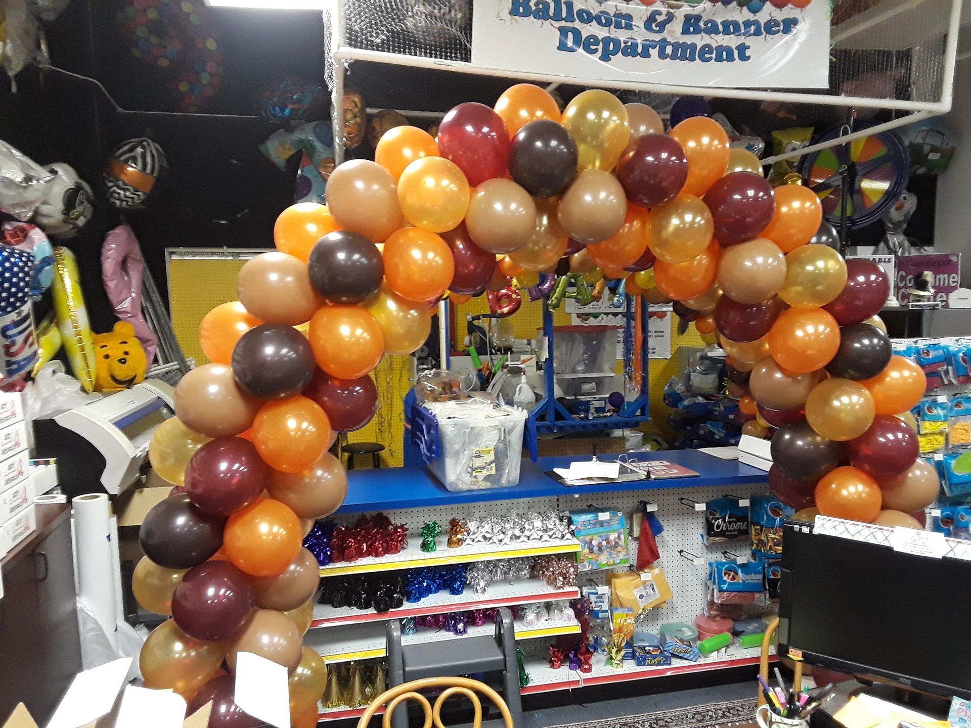 An arch made of orange, brown, and tan balloons framing a store counter in a party supply shop.