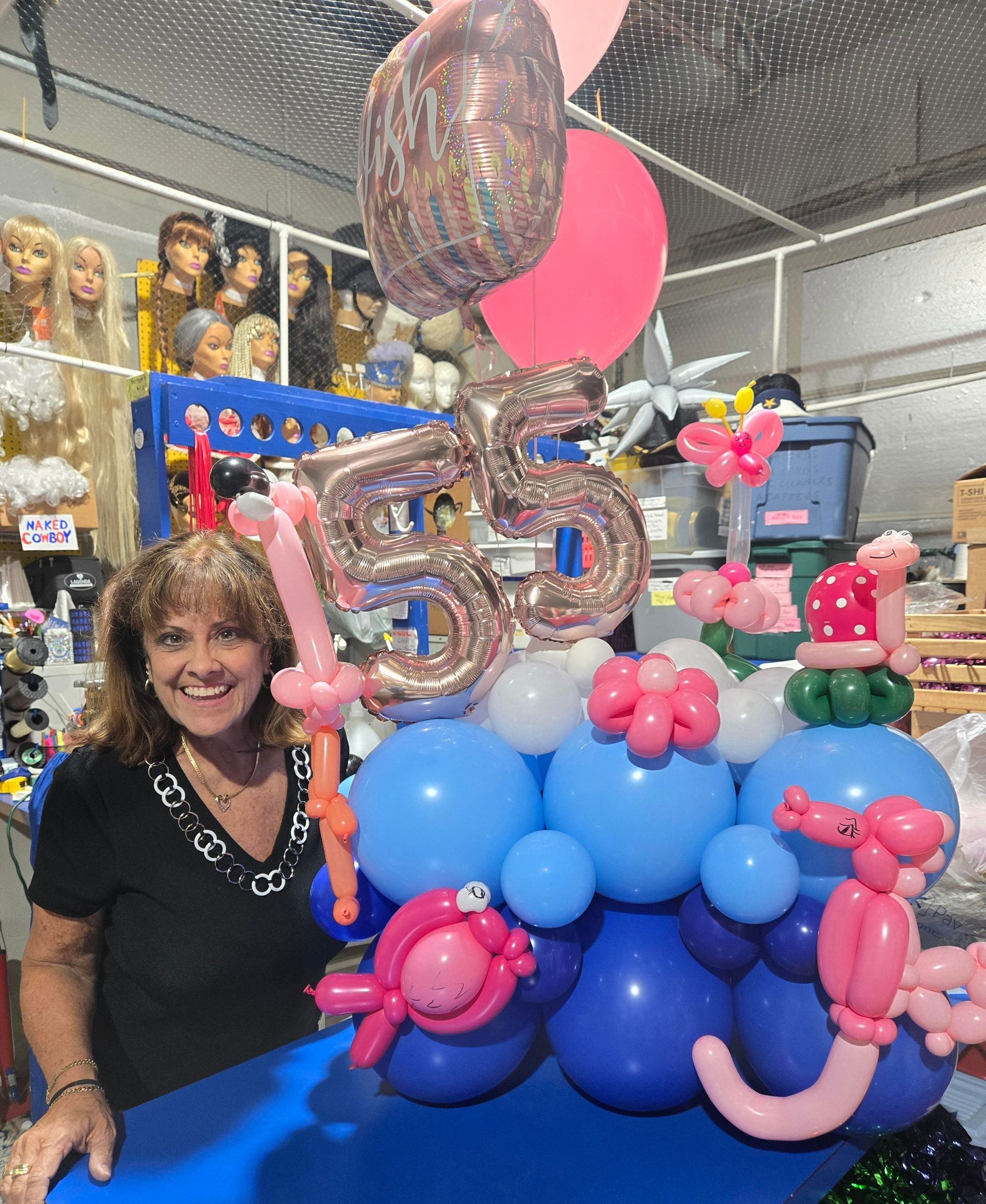 A woman is standing next to a bunch of balloons with the number 55 on it