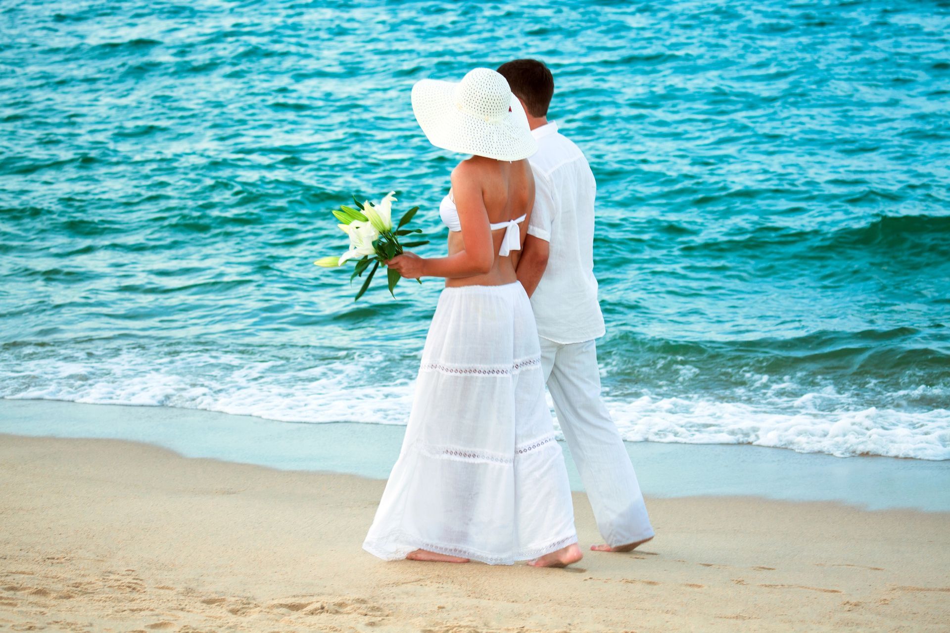 A couple walks along a Florida beach by the water in sunshine. 