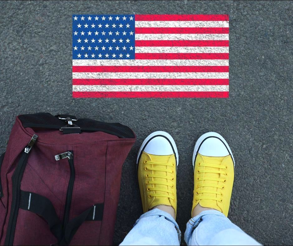 A person with a tote bag points their yellow sneakers toward a drawing of the U.S. flag.