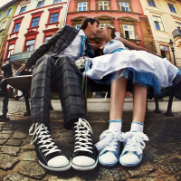 A couple kisses outside on a bench while wearing formal attire and sneakers. 