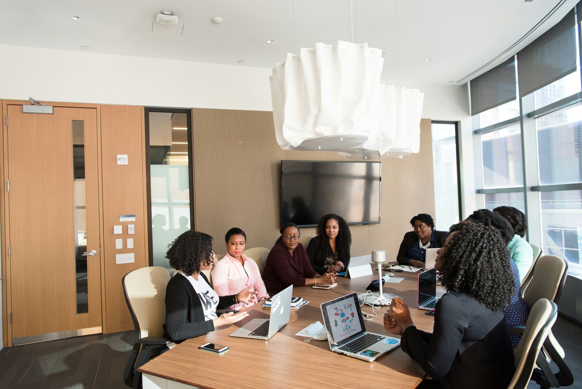 Eight women sit at a conference table in an office environment.