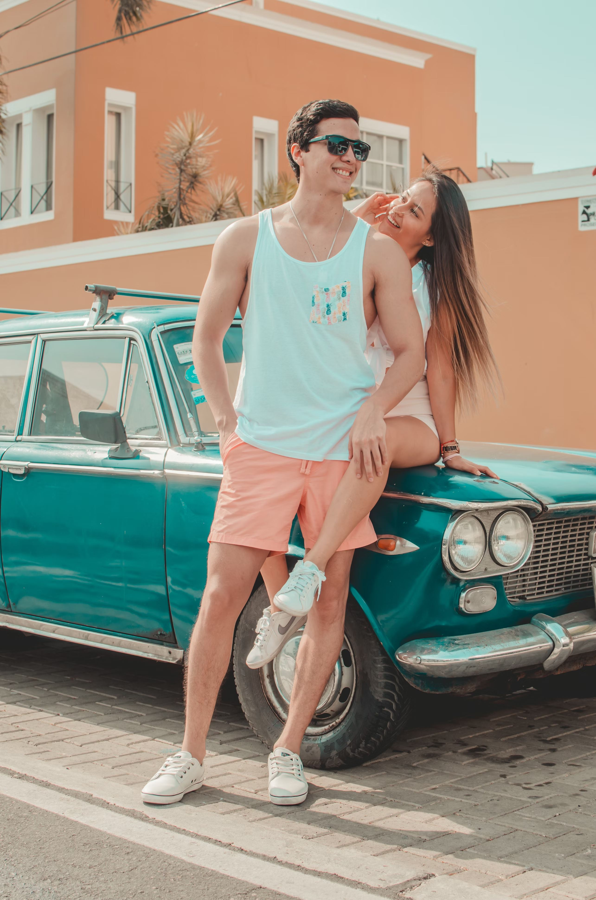 A young couple cuddles near a classic car. 
