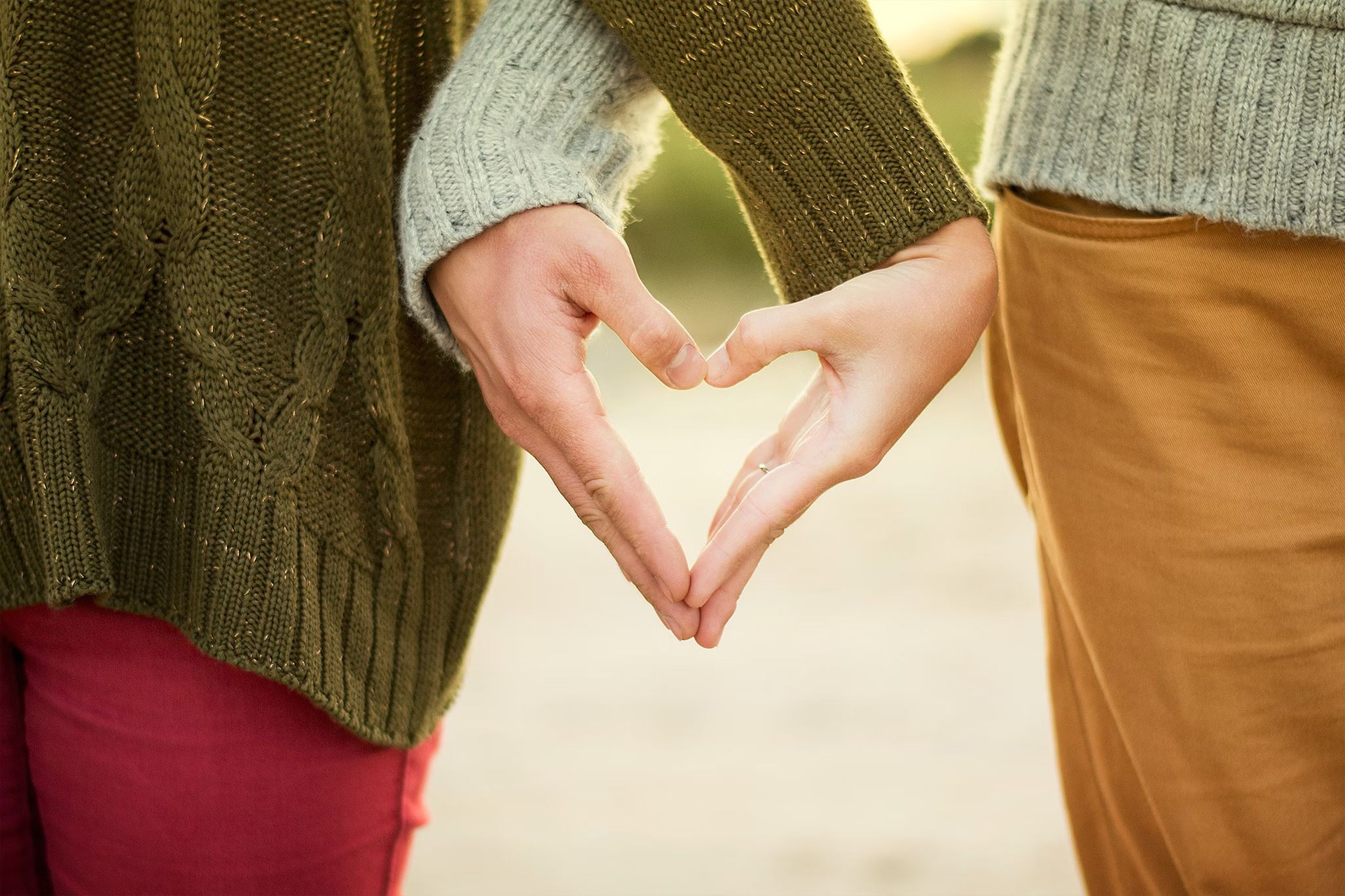 A couple holds hands, and they make the shape of a heart with their hands.