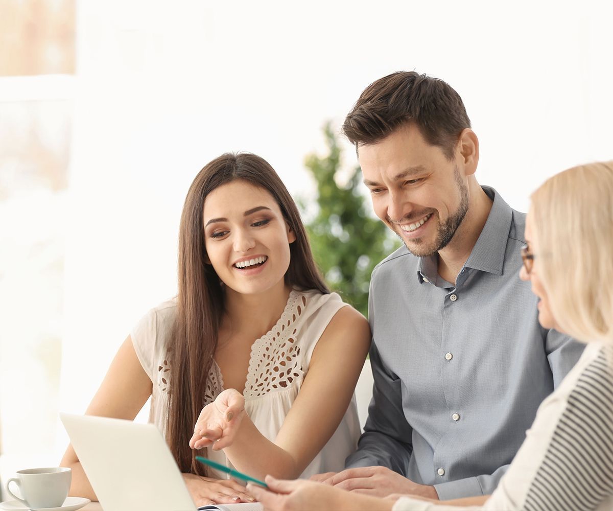 A group of people are sitting around a table looking at a laptop.