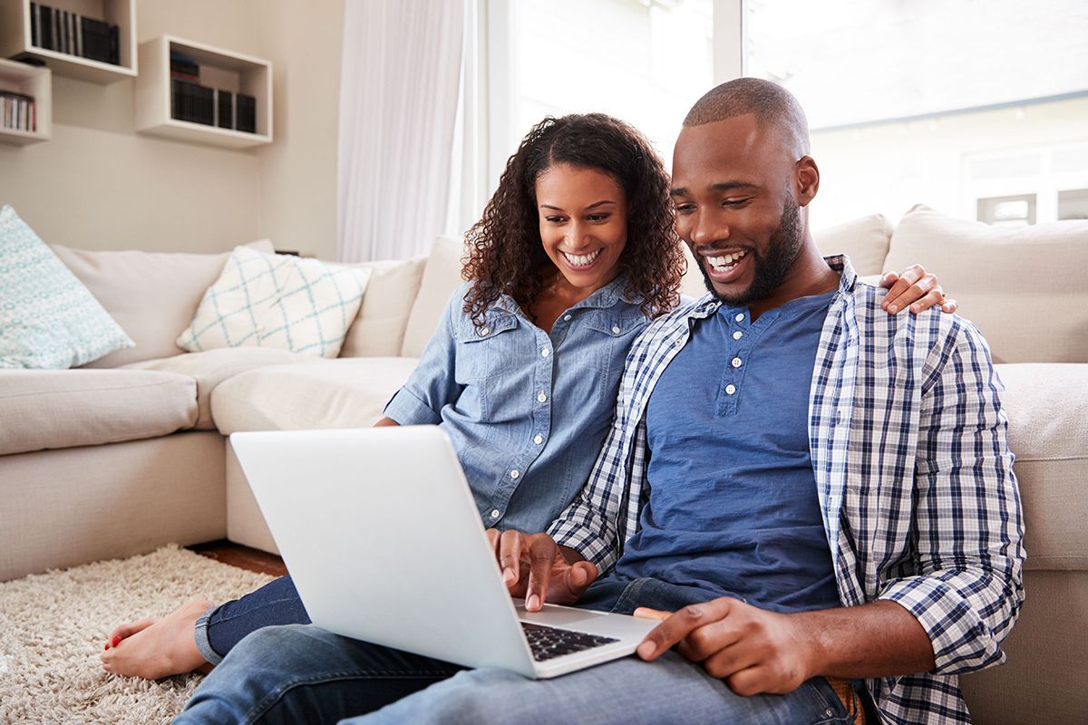A man and a woman are sitting on the floor using a laptop computer.