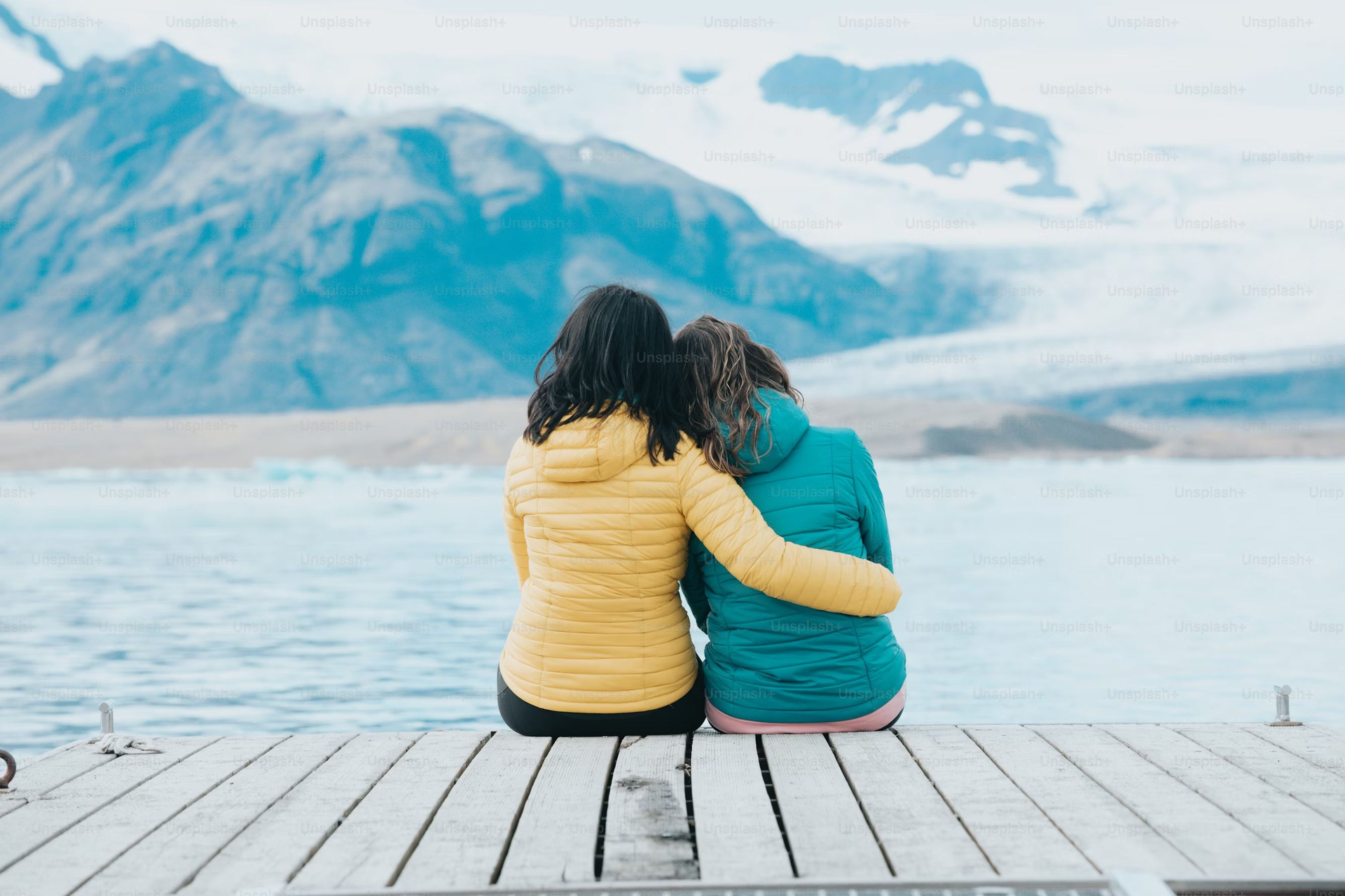 Two women cuddle while sitting on a doc and looking at the lake.