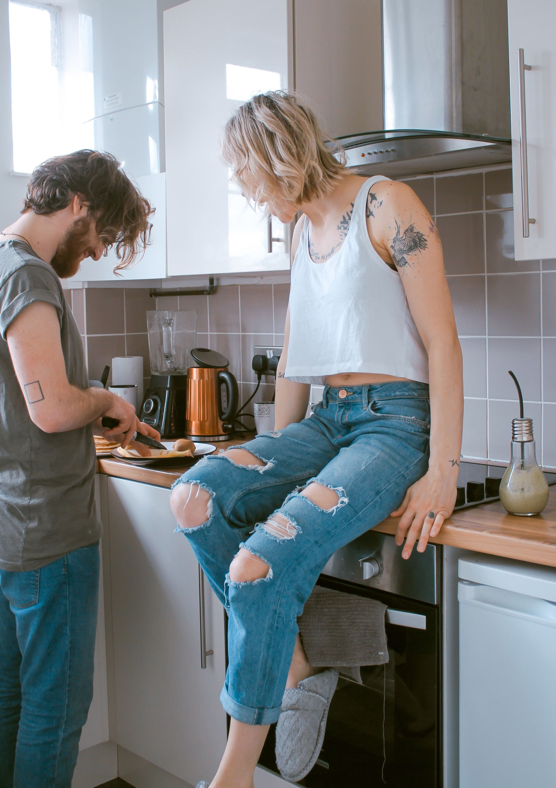 A tattooed couple cooks in the kitchen together. 