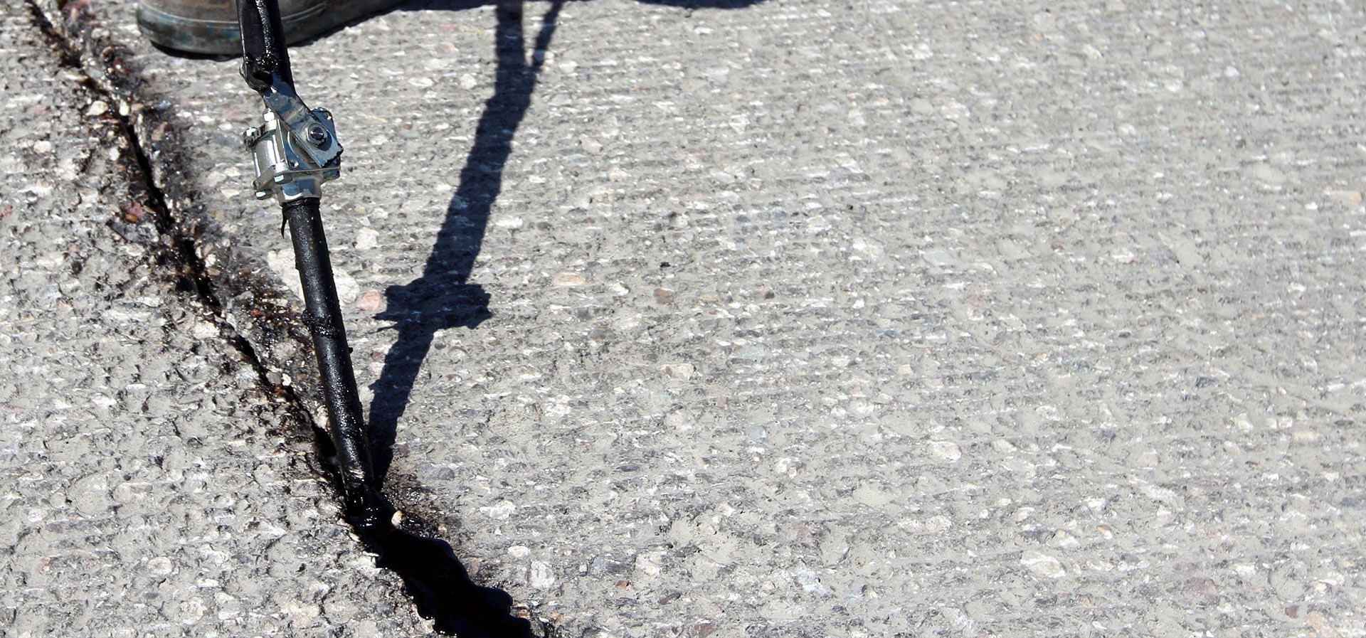 A surveyor's pole stands in a deep crack within a gray concrete surface.