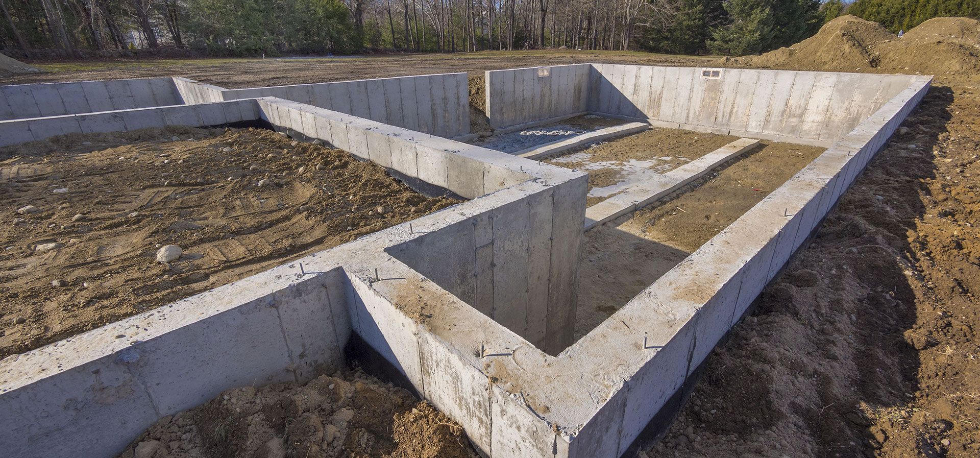 Concrete foundation walls for a new building under construction, set in an excavated plot of dirt.