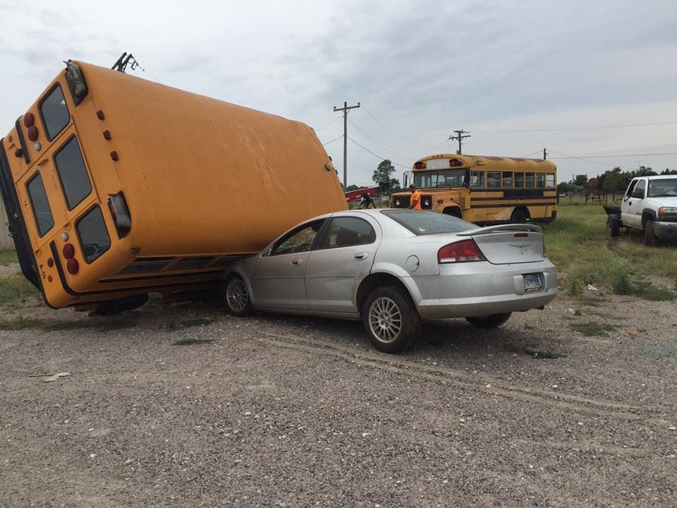 A school bus is upside down on top of a car