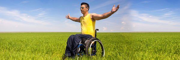 Man in a wheelchair sitting in an open field with his arms outstretched