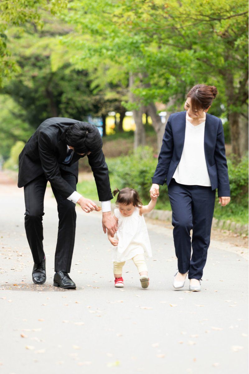 A couple in formal attire walking with their young daughter.