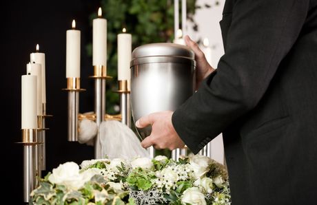 A man is holding a silver urn at a funeral.