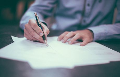 A man is writing on a piece of paper with a pen.