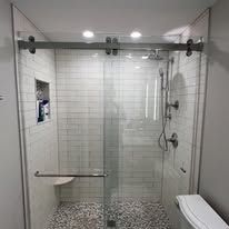 Modern walk-in shower with white subway tile walls, pebble floor, built-in shelf, and a sliding glass door.