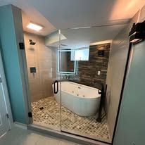 A modern bathroom featuring a white soaking tub inside a glass-enclosed shower with pebble tile flooring.