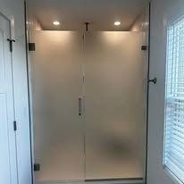 A shower with frosted glass double doors, dark hardware, and two recessed ceiling lights in a bright bathroom.