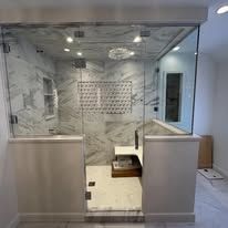 A walk-in shower with white marble walls, glass panels, a bench seat, and recessed lighting in a modern bathroom.