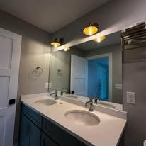 A double-sink bathroom vanity with teal cabinets, white countertops, two wall lights, and a large wall mirror.