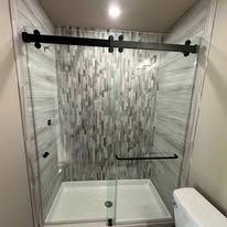 Modern walk-in shower with a glass sliding door, black hardware, and gray textured tile walls.