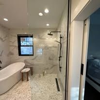 A modern bathroom featuring a white freestanding tub, a glass-enclosed shower, and light-toned marble tile finishes.