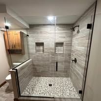 A modern bathroom with a glass-enclosed shower featuring light gray horizontal tile walls and a pebble floor.