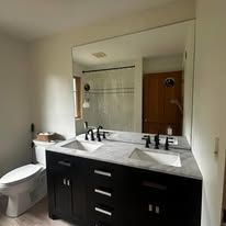 A modern bathroom featuring a dark wood double-sink vanity with a white countertop and a large, frameless wall mirror.