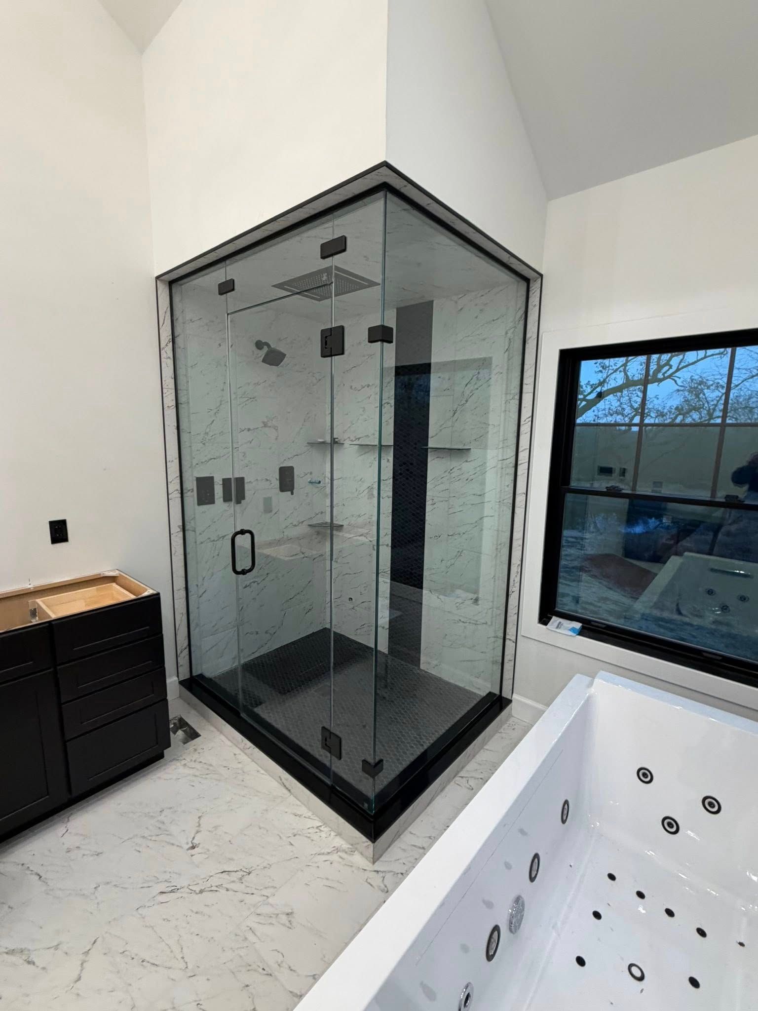 A modern bathroom featuring a glass-enclosed corner shower with black hardware next to a white jetted bathtub.