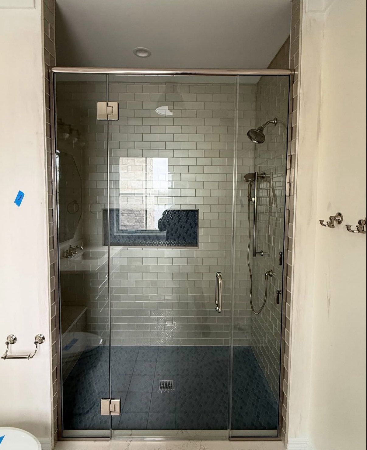 A glass-enclosed shower with subway tile walls, a dark blue tiled floor, and chrome fixtures in a modern bathroom.