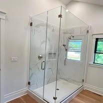 A frameless glass shower enclosure with marble-patterned tile, chrome hardware, and a window in a modern bathroom.