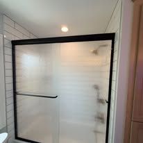 A frosted glass shower door with a black frame installed in a white subway-tiled bathroom.