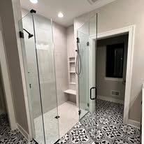 A modern walk-in shower with glass doors, a built-in niche, and patterned black-and-white tile flooring.