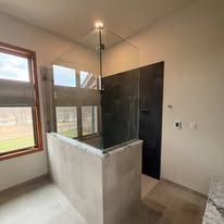 A modern bathroom with a glass-enclosed shower featuring dark stone tiles, set against a window and light-colored walls.